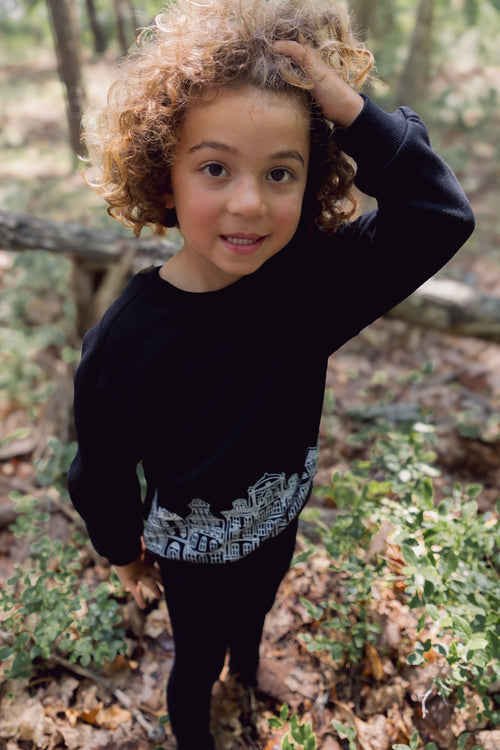 Child wearing a black Skyline Sweatshirt with white cityscape graphic in a forest setting.