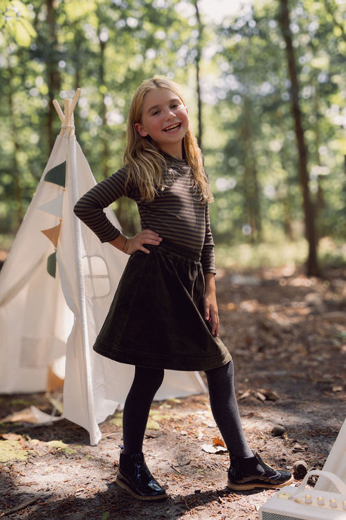Forest green corduroy A-line skirt with elastic waistband on a smiling girl outdoors.