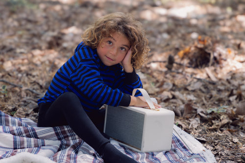 Boy wearing Striped Sweatshirt - Blue &amp; Black outdoors on a plaid blanket beside a portable speaker.