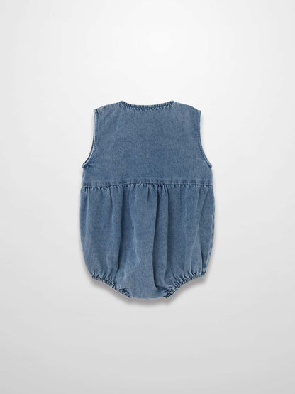Back view of blue denim romper with sleeveless design, gathered waist, and elastic leg openings.