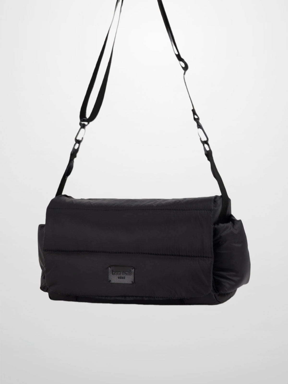 Black padded diaper bag with foldover flap, adjustable crossbody straps, minimalist accessory for modern parents.