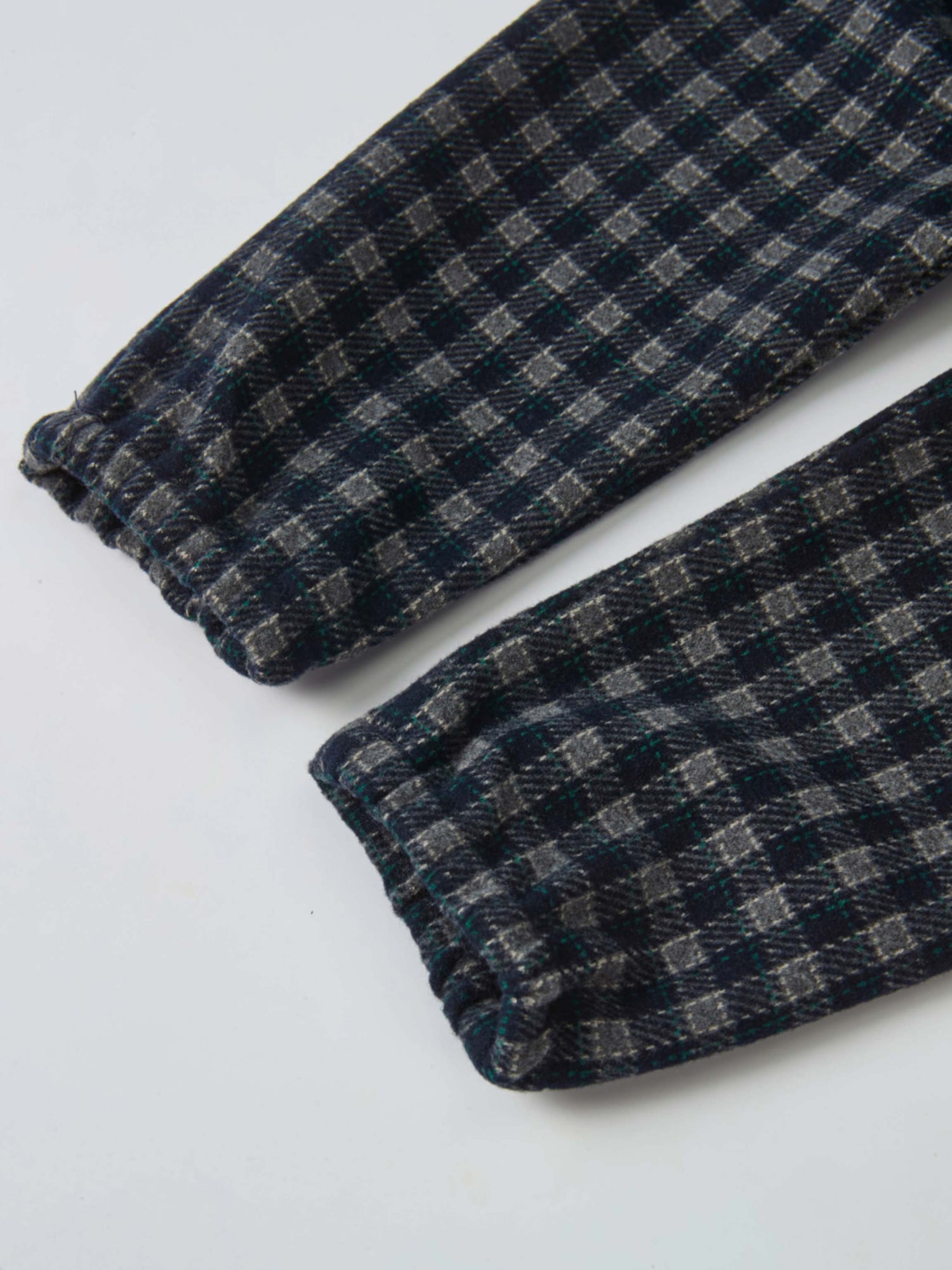 Girls plaid overalls fabric close-up in navy with grey and green checks, cuffed hems
