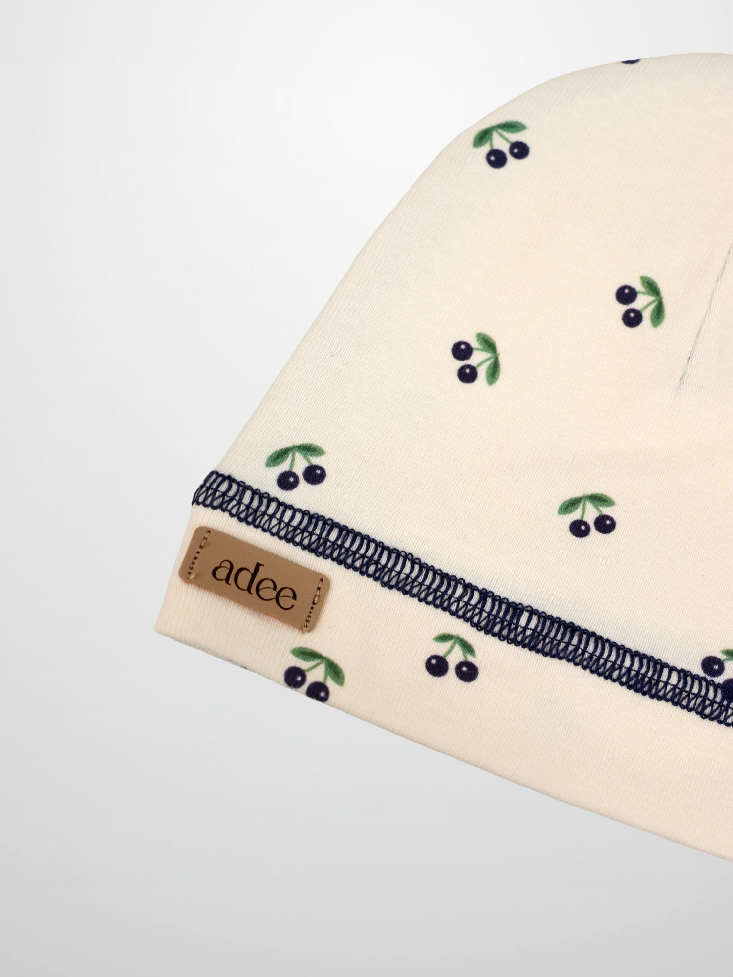 Blue Cherry Hat by Adee, cream knit with blue cherry print and green leaves; navy stitched edge