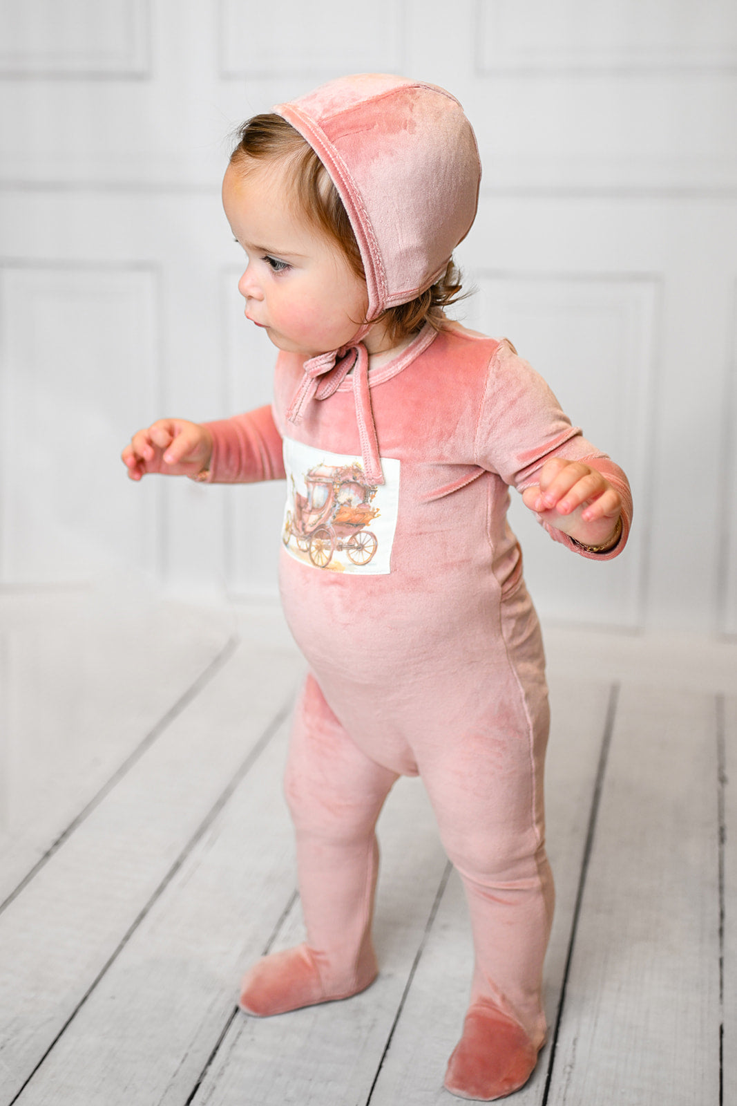 Velour Carriage Stretchy - Pink: baby girl in pink velour footed romper with vintage carriage patch, hooded with a bow.