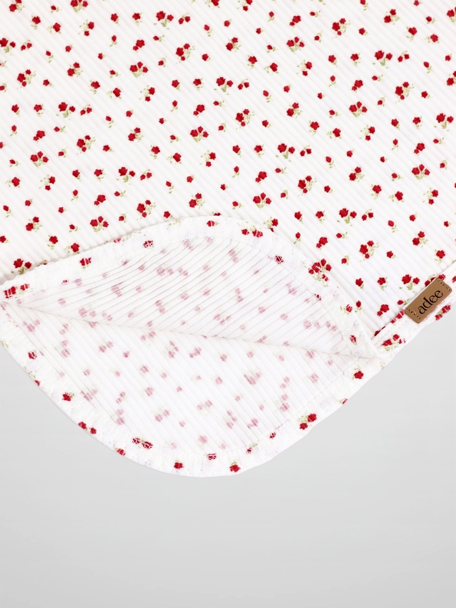 Red flower swaddle blanket for girls by Adee, a white receiving blanket with tiny red blooms.