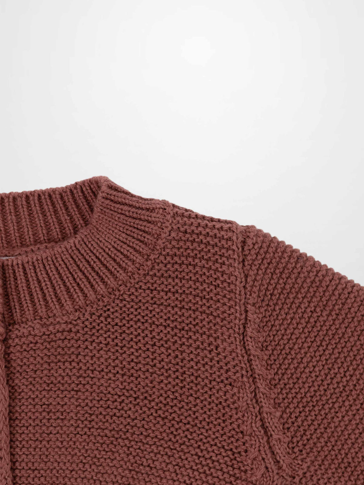 Cropped cardigan for girls in pink knit with a ribbed neckline and textured weave, close-up soft, chunky knit texture