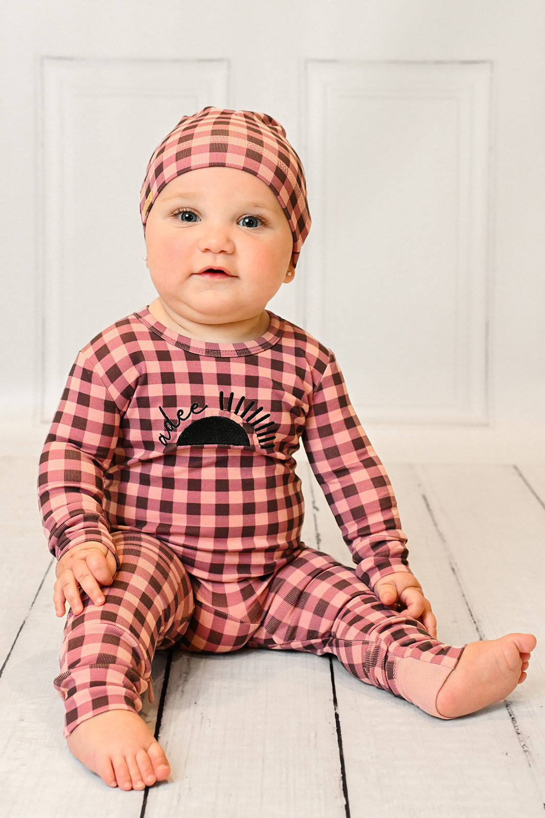 Baby girl in pink gingham stretchy footie with sun embroidery and Adee on front, inseam zipper.