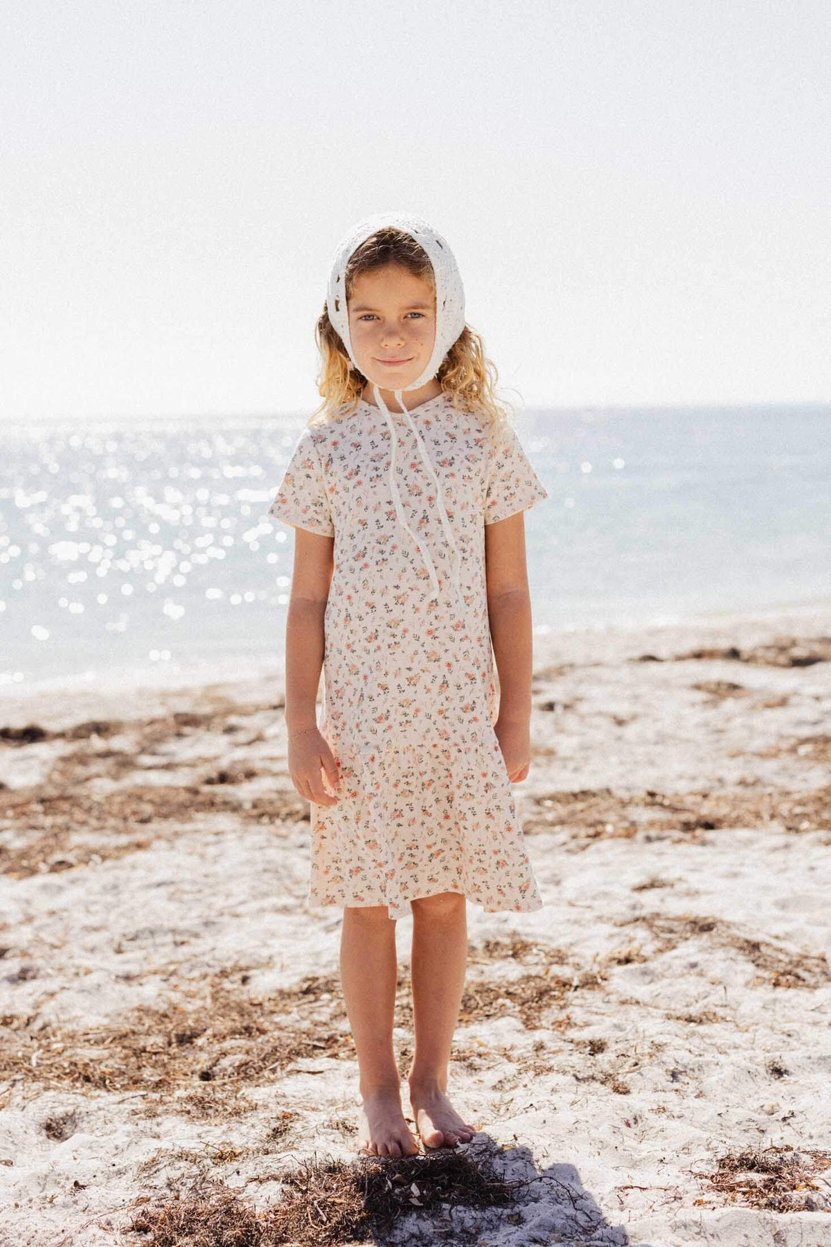 Little girl in an off-white dress with hand-painted pink flowers and leaves, short bubble sleeves, at the beach.