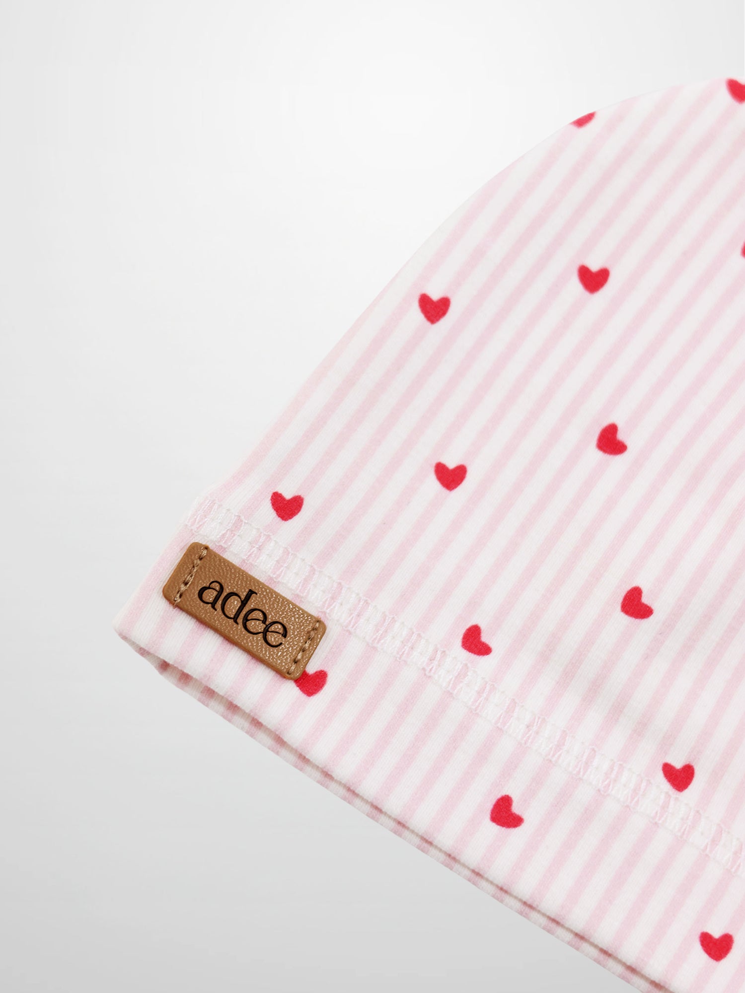 Pink heart hat for girls; pink striped fabric with red hearts and Adee brand tag.