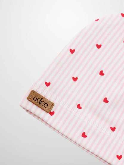 Pink heart hat for girls; pink striped fabric with red hearts and Adee brand tag.