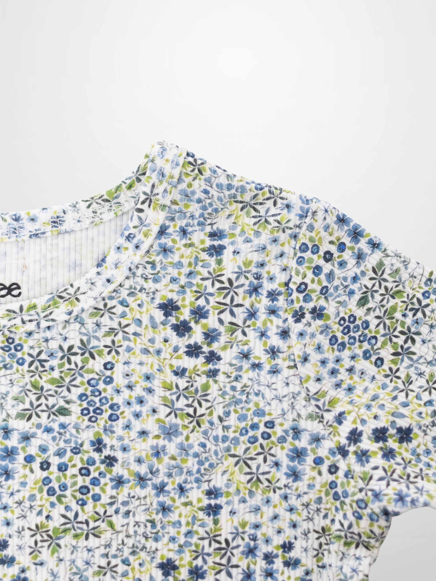 Blue floral pajamas top with small blue flowers and green leaves on white fabric.