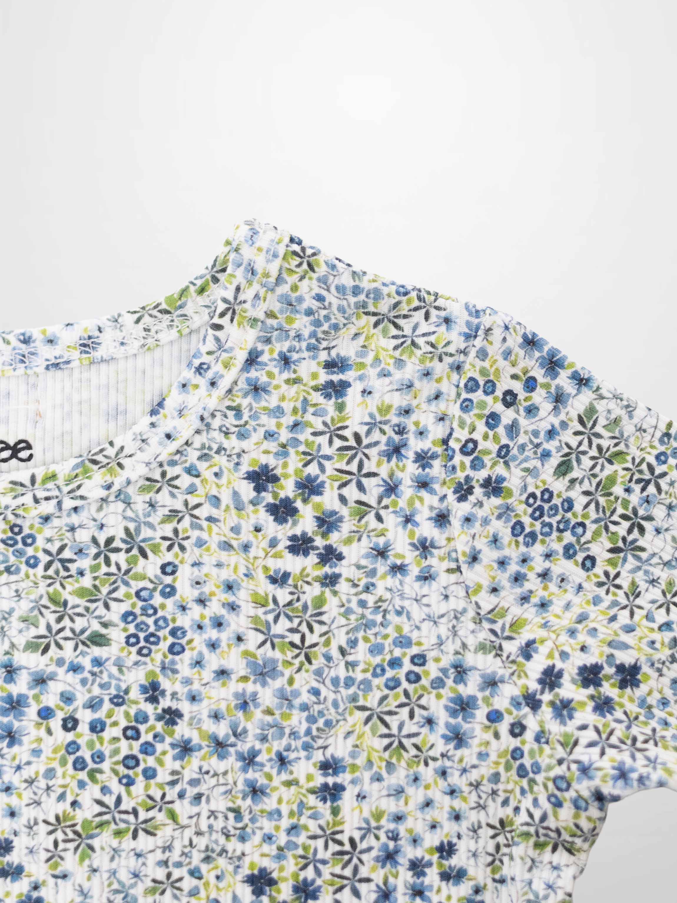 Blue floral pajamas top with small blue flowers and green leaves on white fabric.