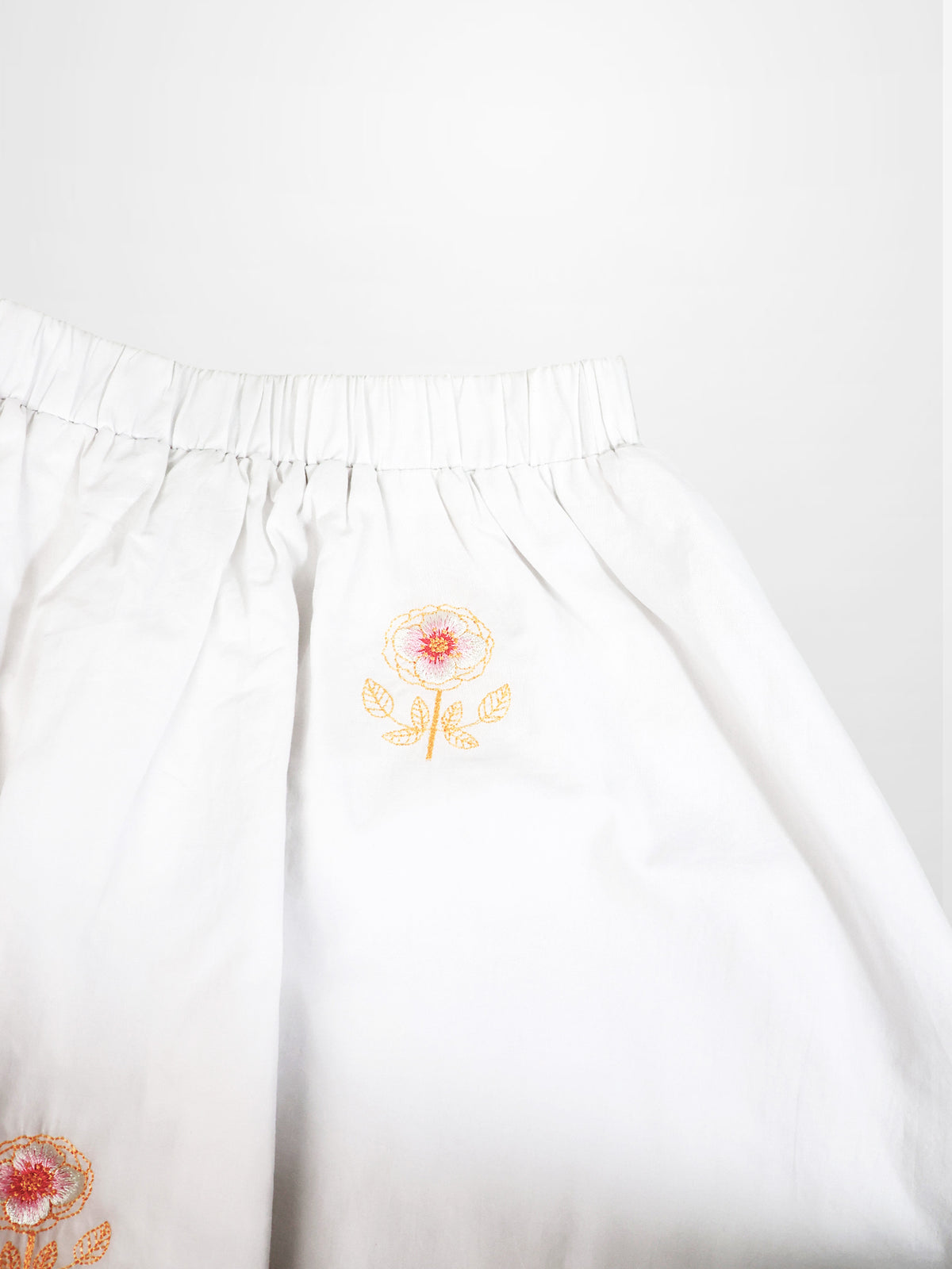 Adee Embroidered Flower Skirt for girls, white fabric with orange flower embroidery and elastic waistband.