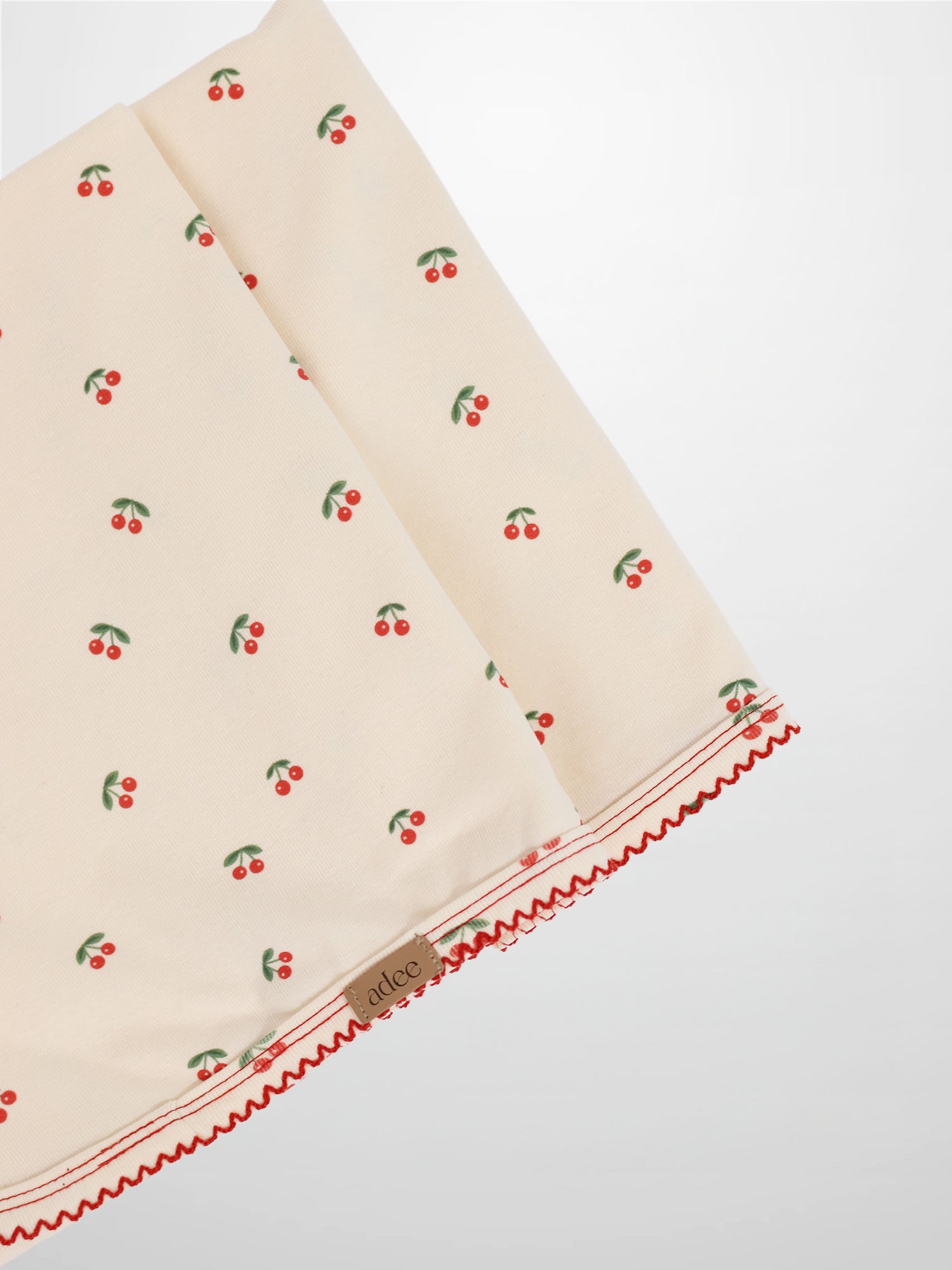 Red Cherry swaddle blanket for girls by Adee with lace trim on cream fabric and scattered cherries.