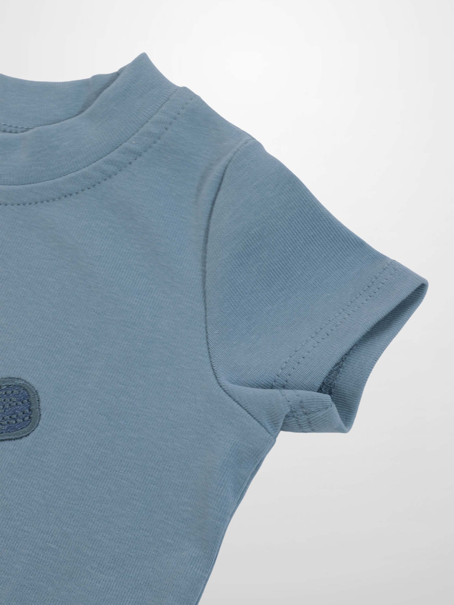 Light blue baseball T-shirt close-up of shoulder and short sleeve with a small circular chest patch.