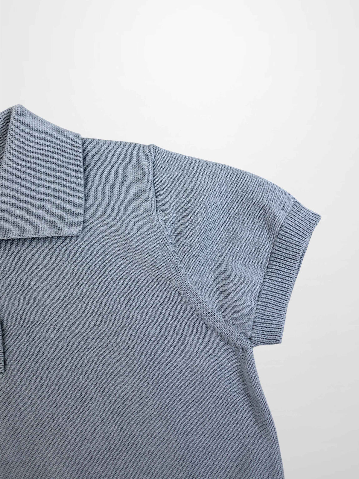 Light blue knit sweater shoulder close-up with ribbed sleeve cuff and polo collar.