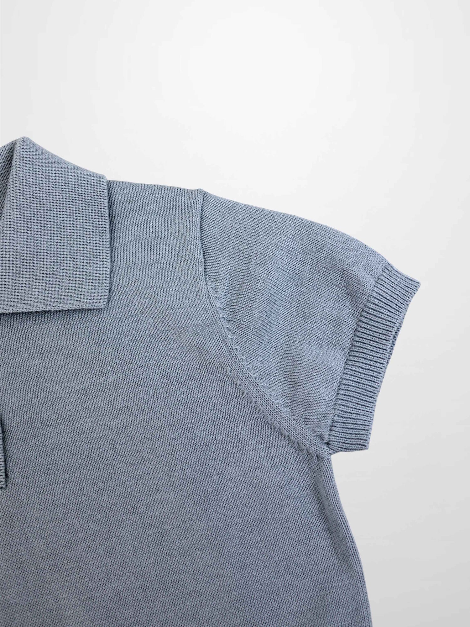 Light blue knit sweater shoulder close-up with ribbed sleeve cuff and polo collar.