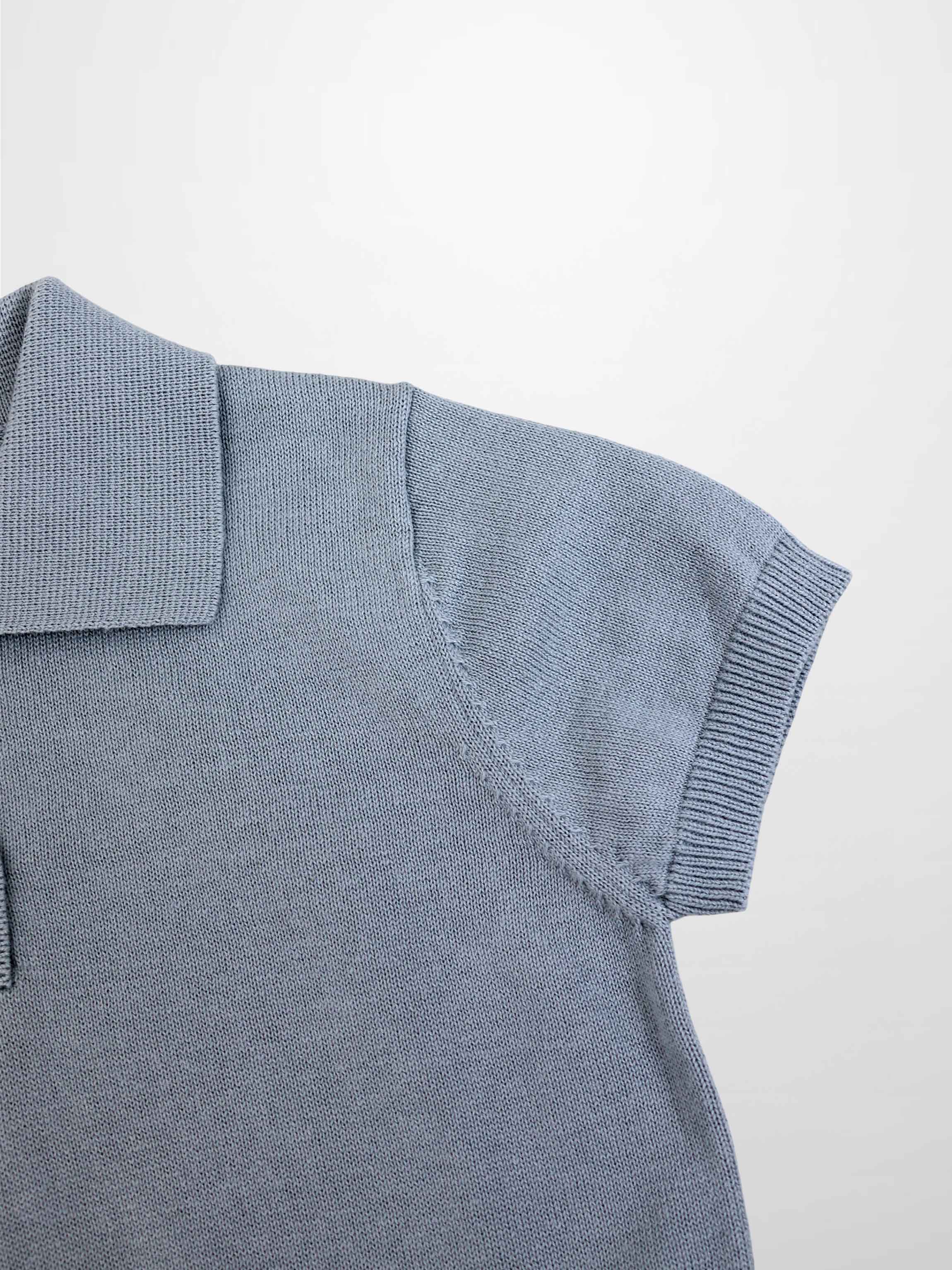 Light blue knit sweater shoulder close-up with ribbed sleeve cuff and polo collar.