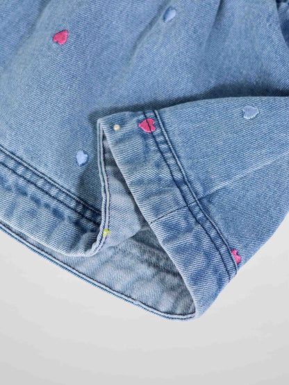 Close-up of light-wash denim with pink and blue heart embroidery on the fabric.