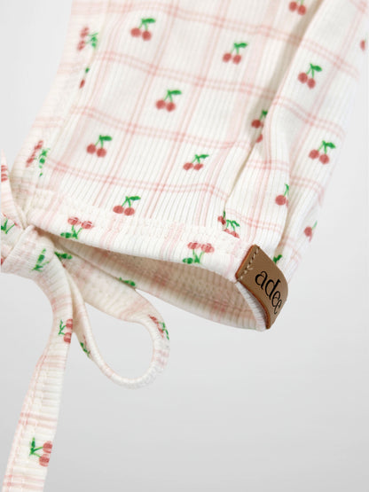 Cherry Window Bonnet for girls by Adee; light pink plaid with cherry prints, ribbed knit, tie closure