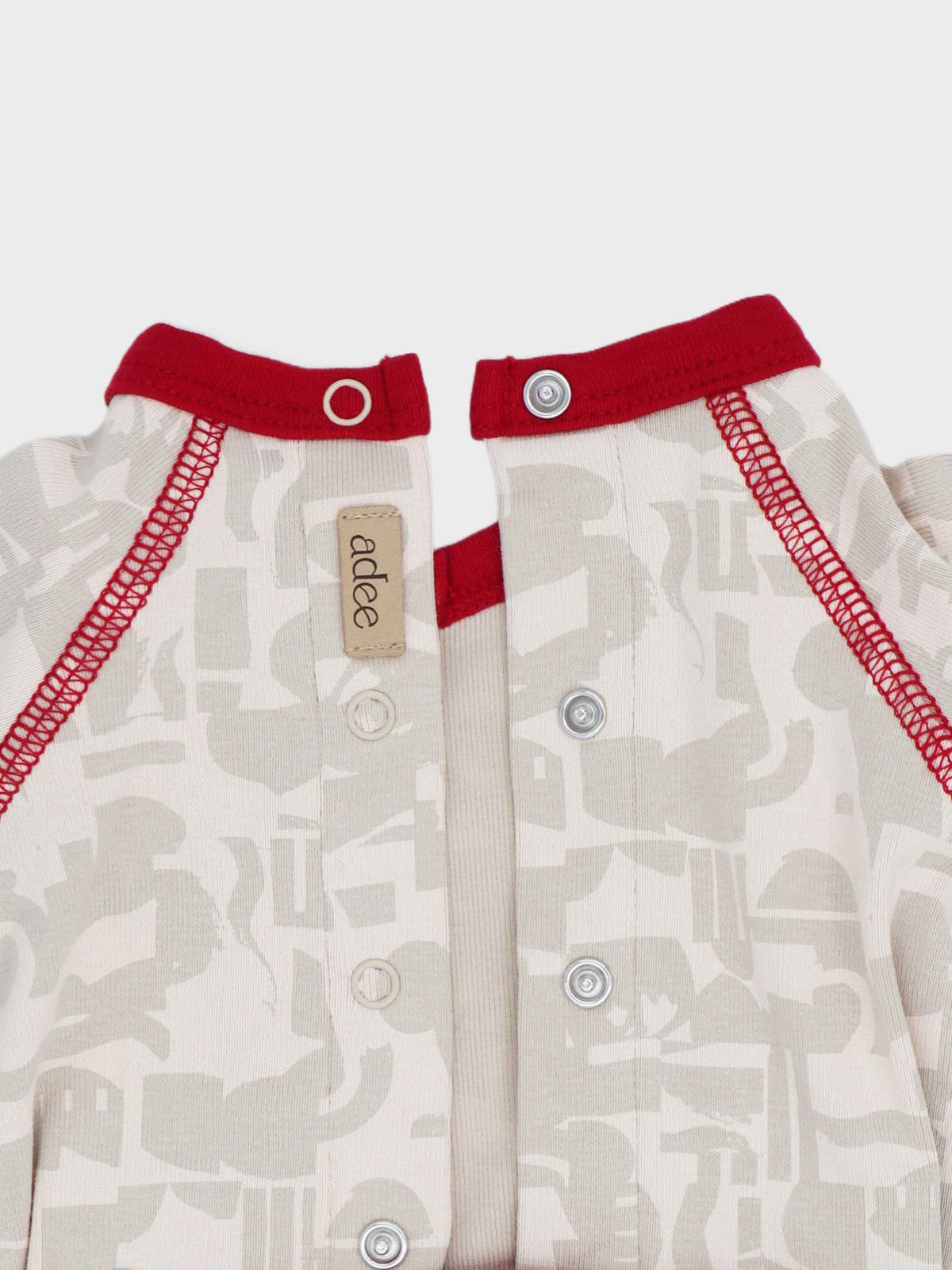 Abstract print baby jumpsuit with red trim and stitching, cream neutrals, front snaps.