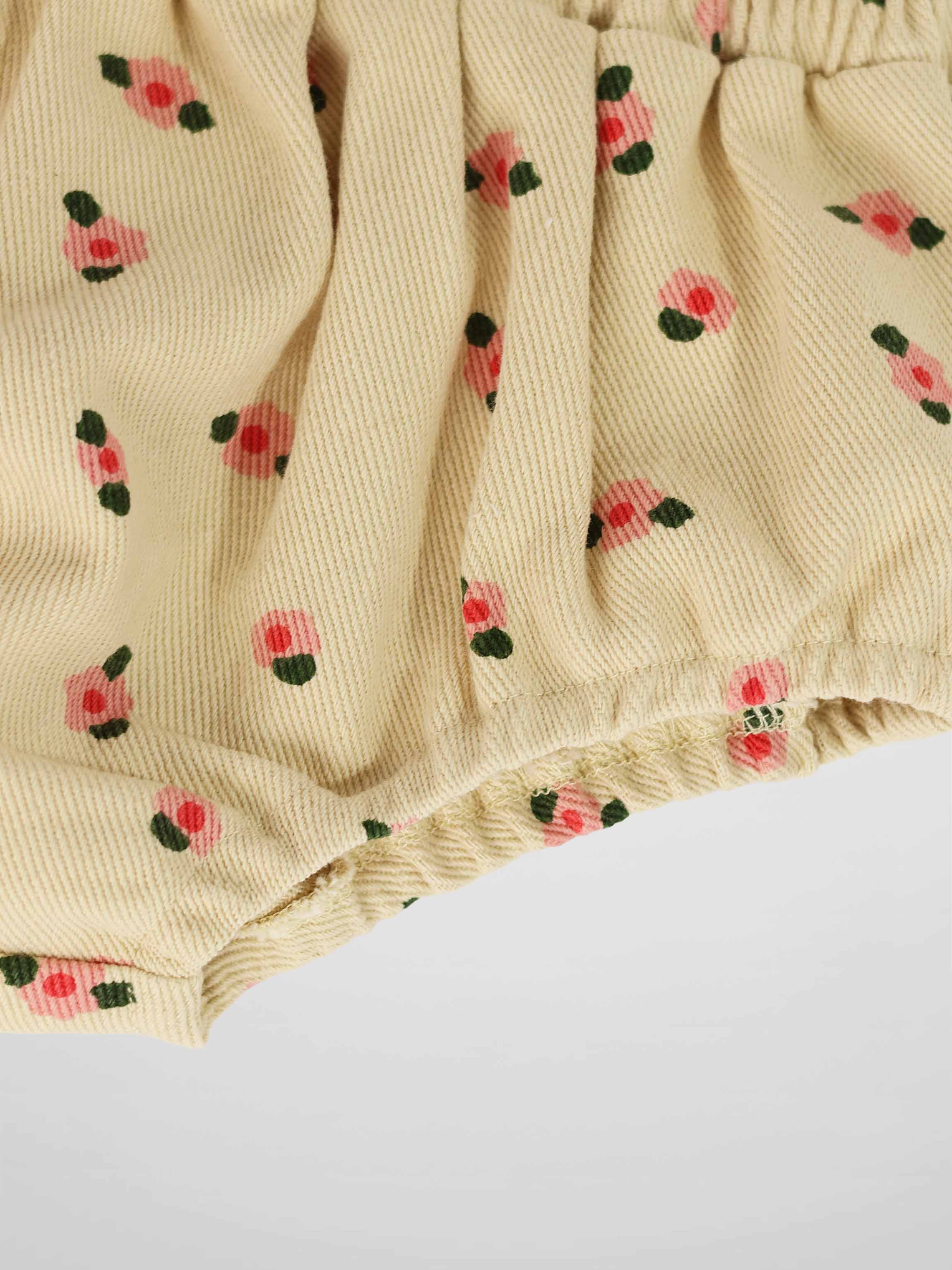Tan floral bloomers fabric close-up with pink blossoms, green leaves, and an elastic waistband.