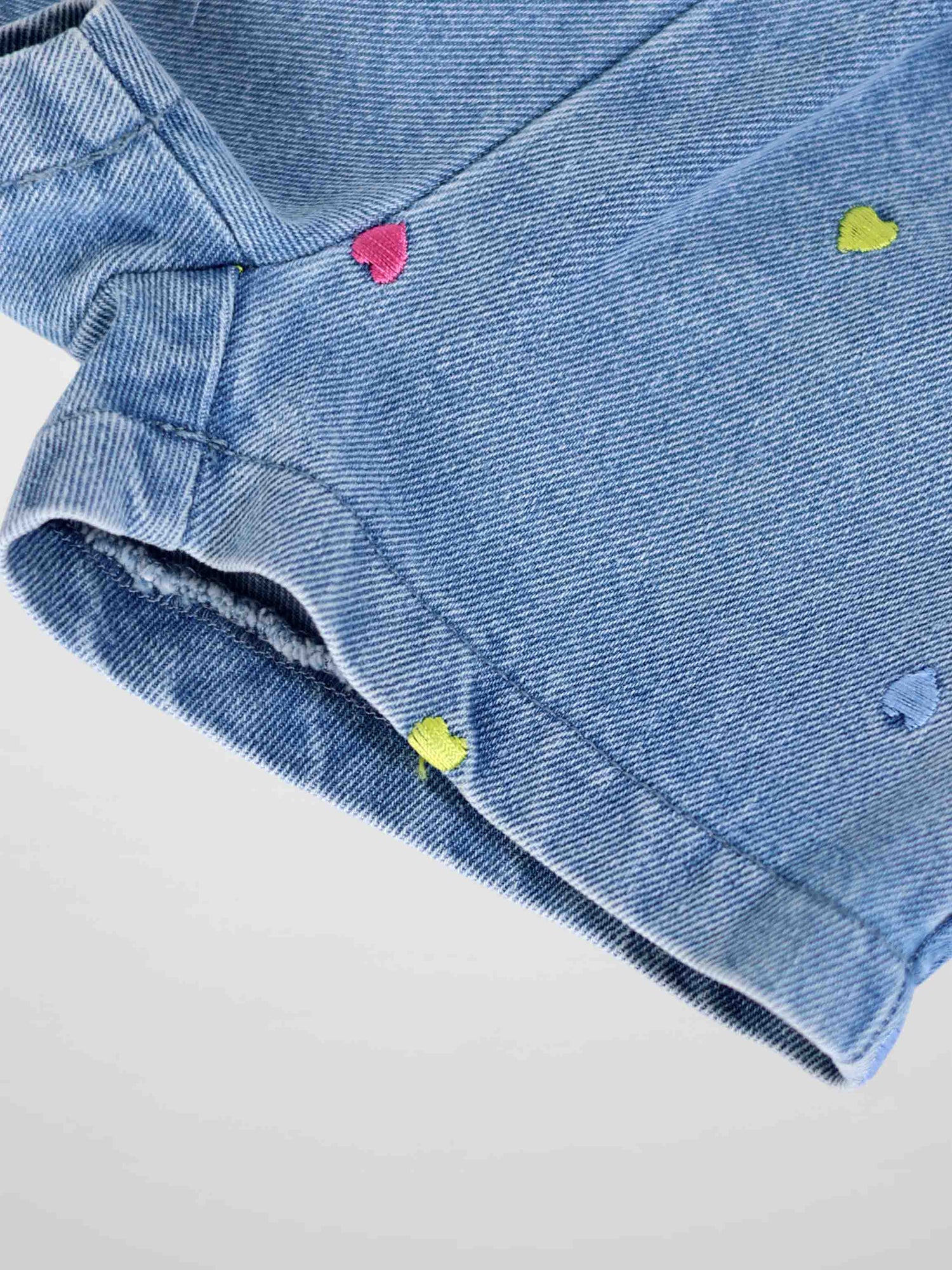 Close-up of light-wash denim shorts with colorful embroidered hearts scattered across fabric