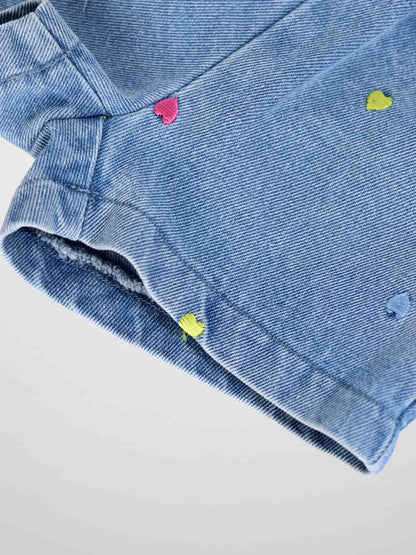 Close-up of light-wash denim shorts with colorful embroidered hearts scattered across fabric