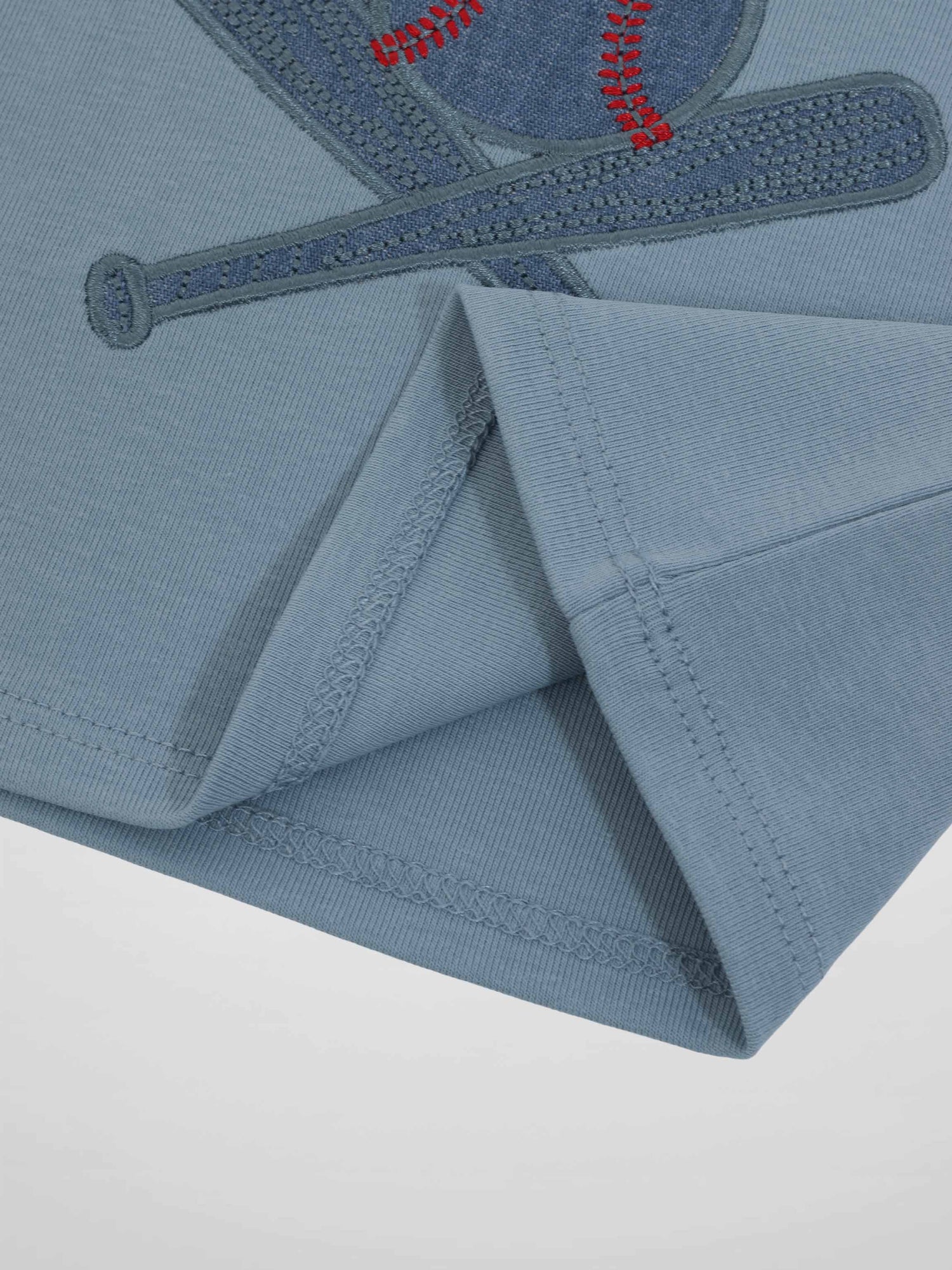 Blue baseball T-shirt with embroidered baseball and bat motif, close-up seam detail.