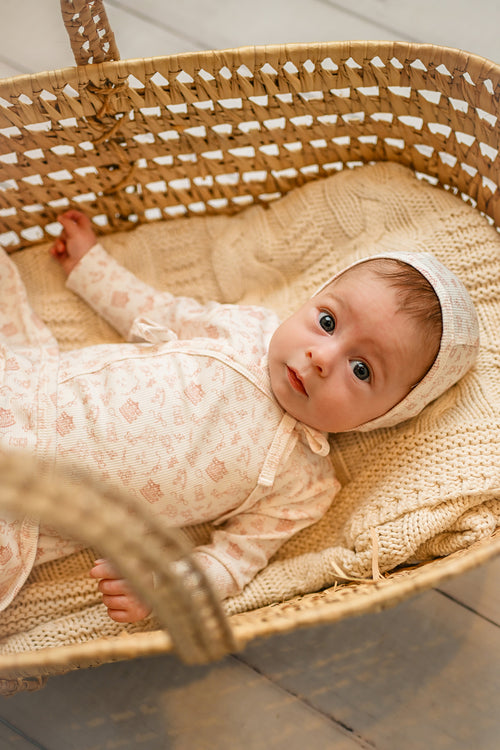 Little Storybook Stretchy - Pink baby jumpsuit worn by a baby girl resting in a woven basket on a knitted blanket.