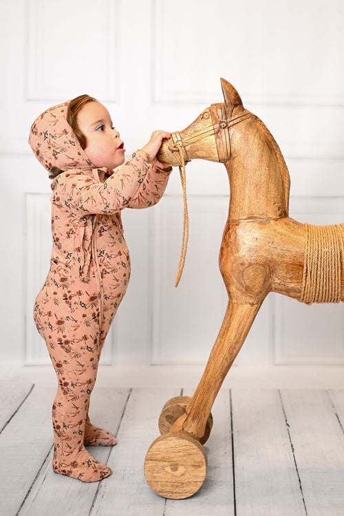 baby girl excited looking cute with a pink jumpsuit and bonnet hat holding a horse 