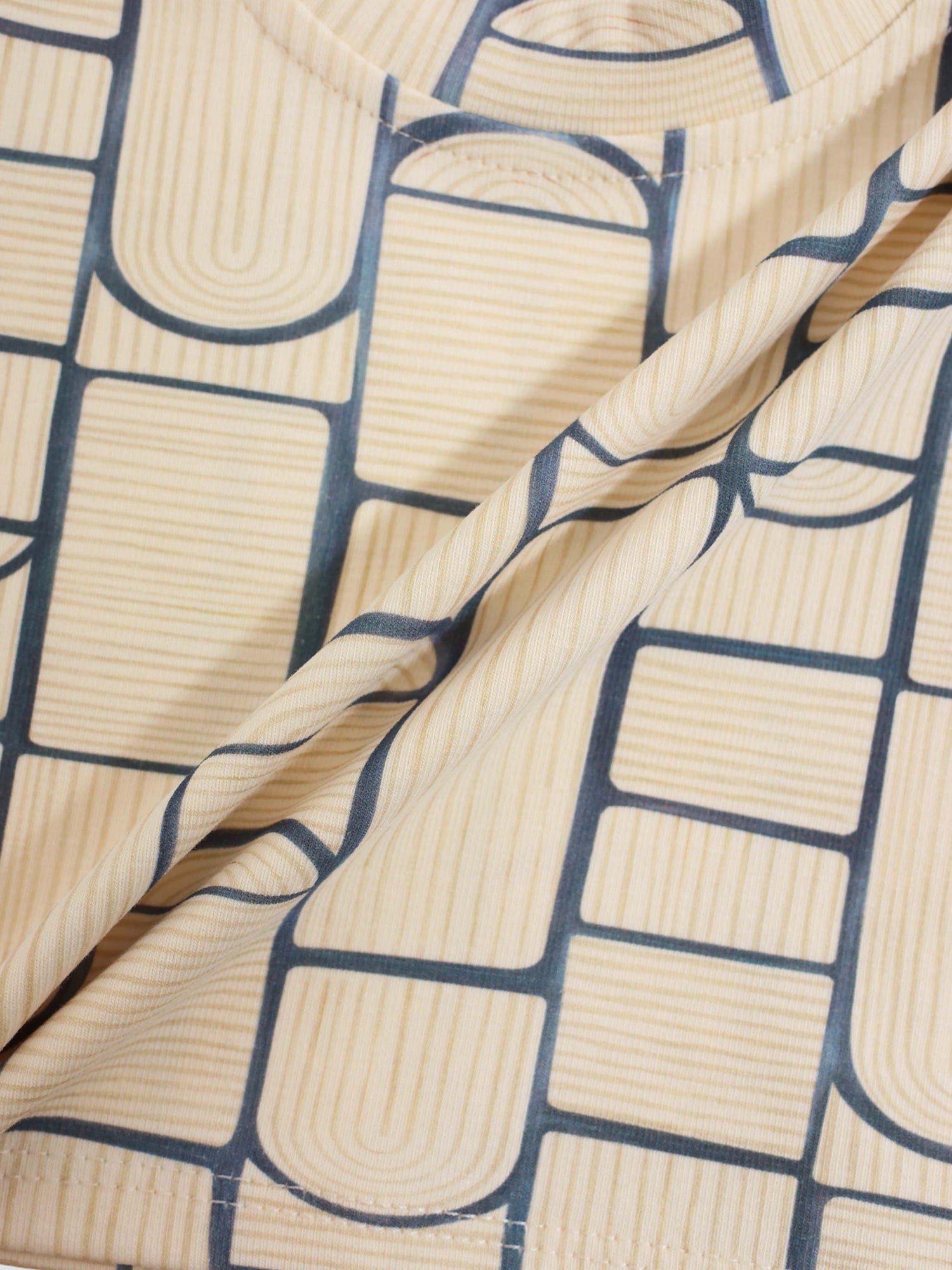 Abstract T-shirt, beige fabric with navy blue geometric grid pattern.