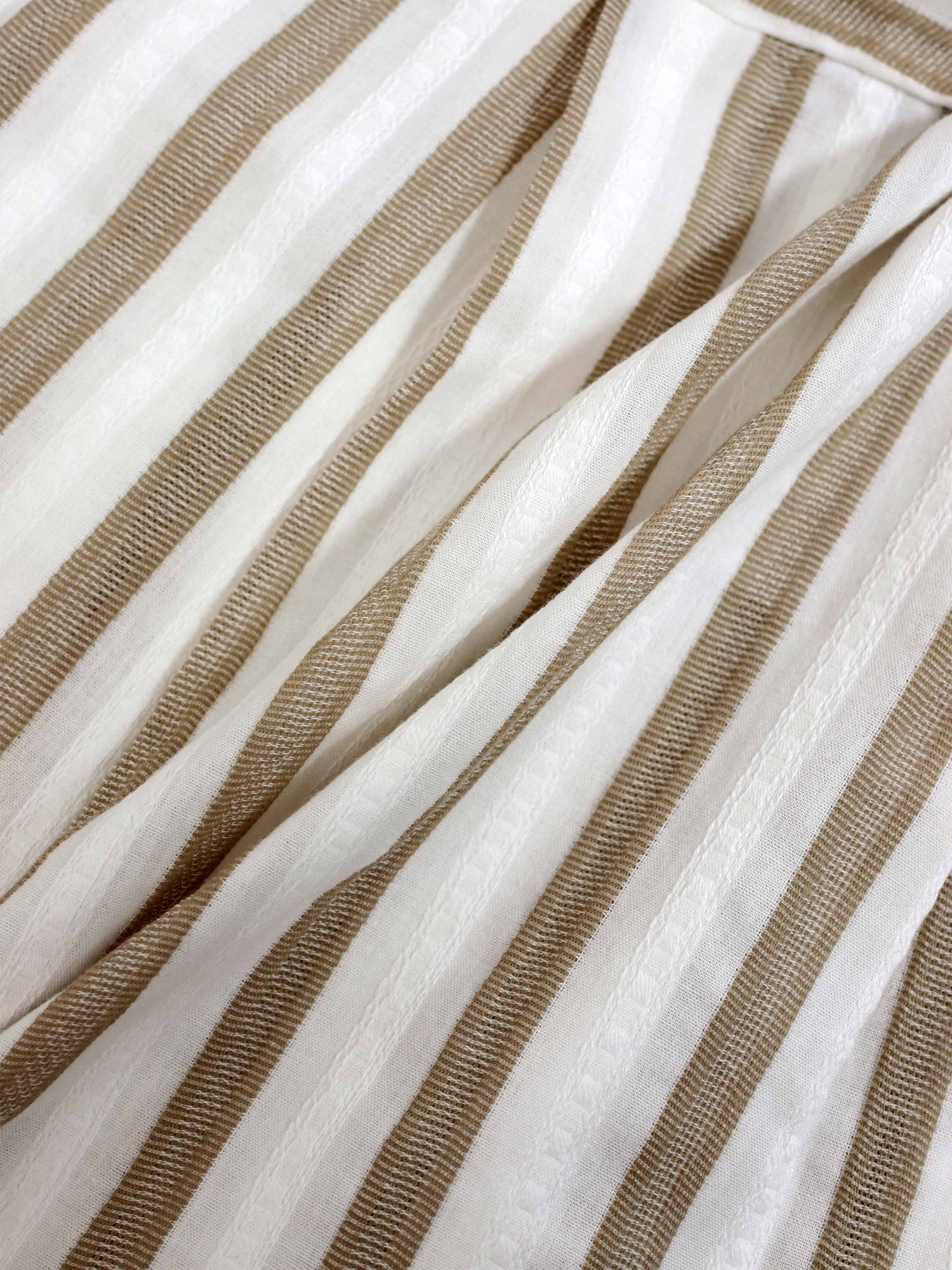 Tan and white striped romper fabric close-up with a textured weave.