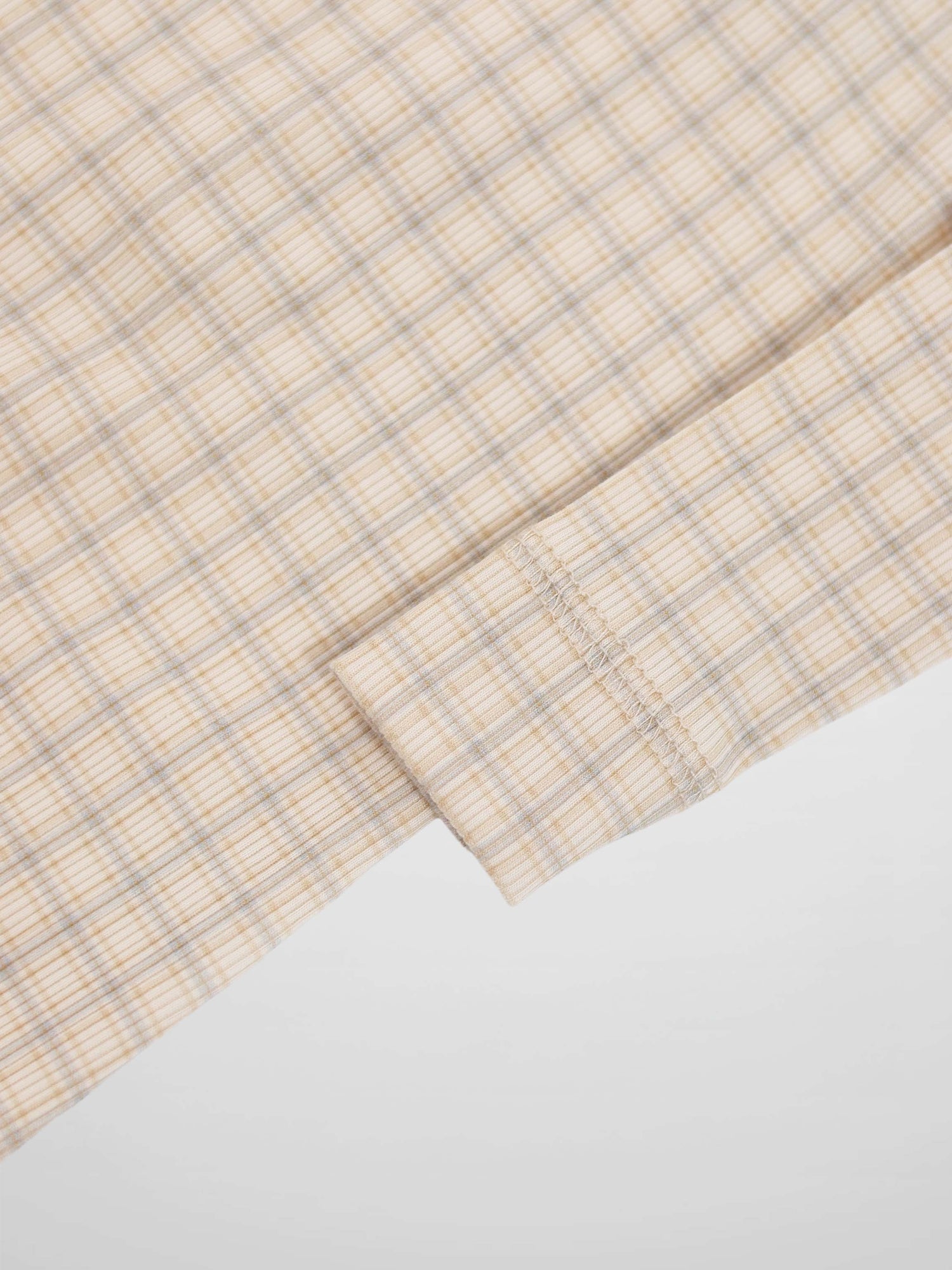 Beige baby jumpsuit fabric with light blue grid plaid and a stitched cuff seam
