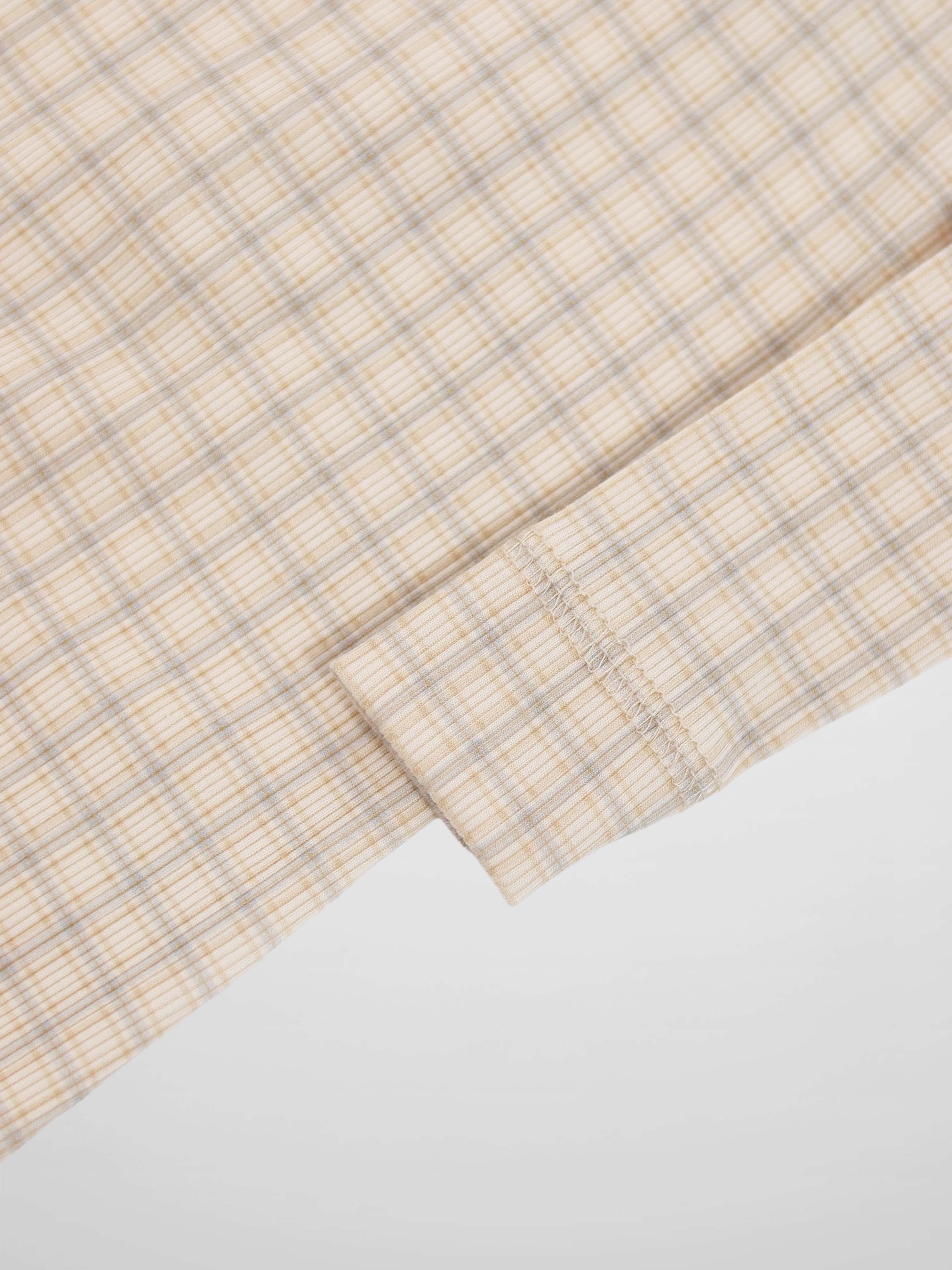 Beige baby jumpsuit fabric with light blue grid plaid and a stitched cuff seam