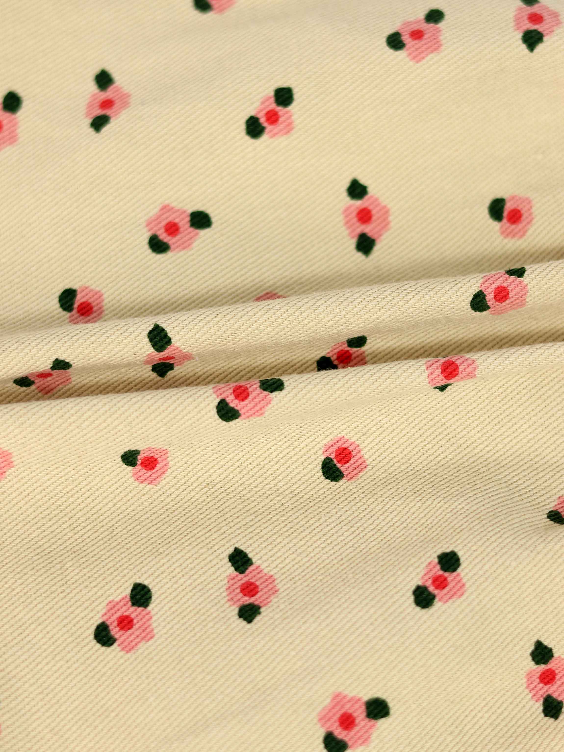 Tan floral shorts fabric with tiny pink blossoms and dark green leaves on a beige background.