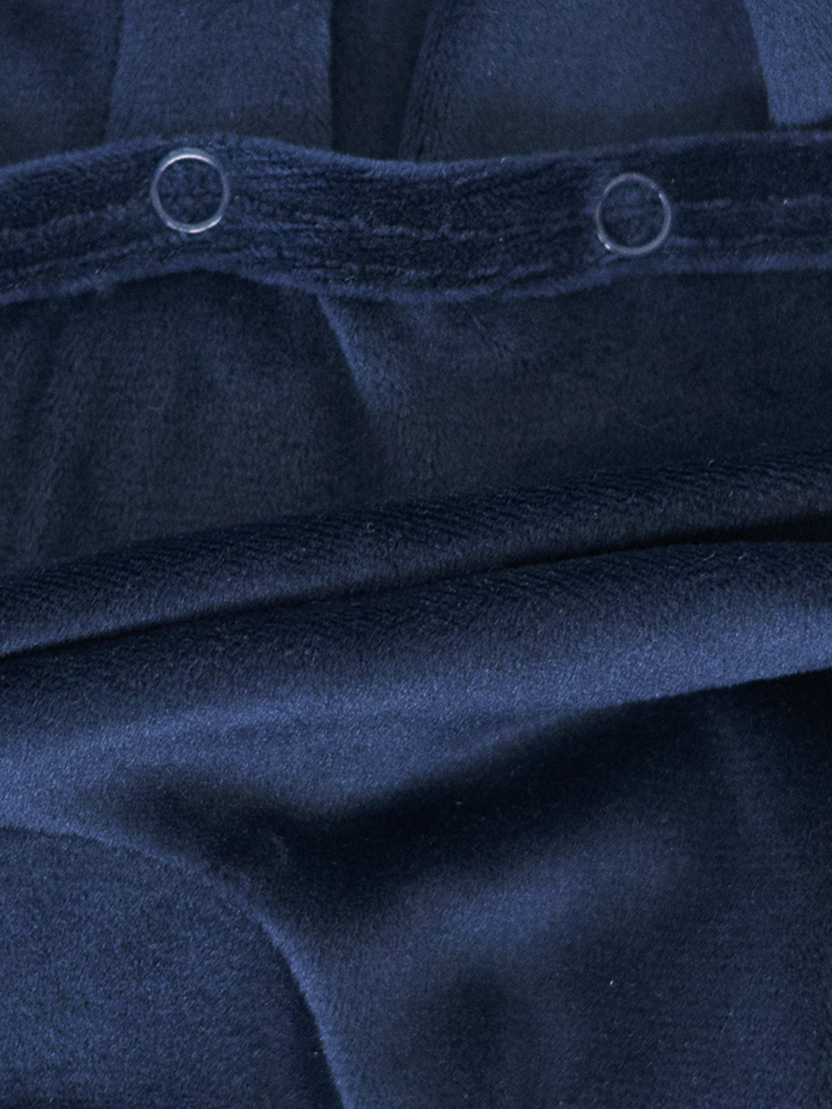 Close-up of navy velour fabric with metal snap closures, part of a baby footie.