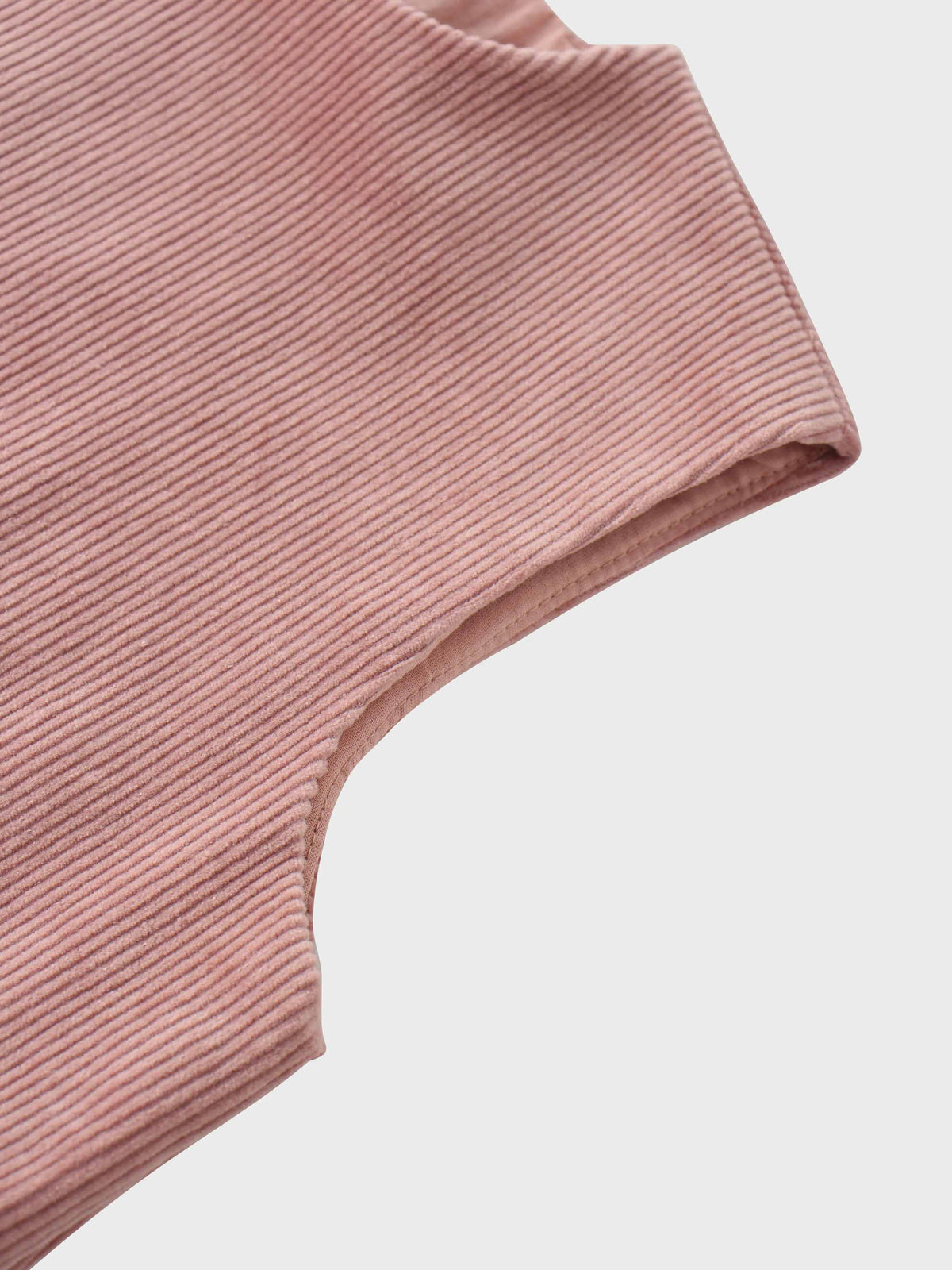Close-up of mauve corduroy fabric with fine ribbed texture and curved hem edge.