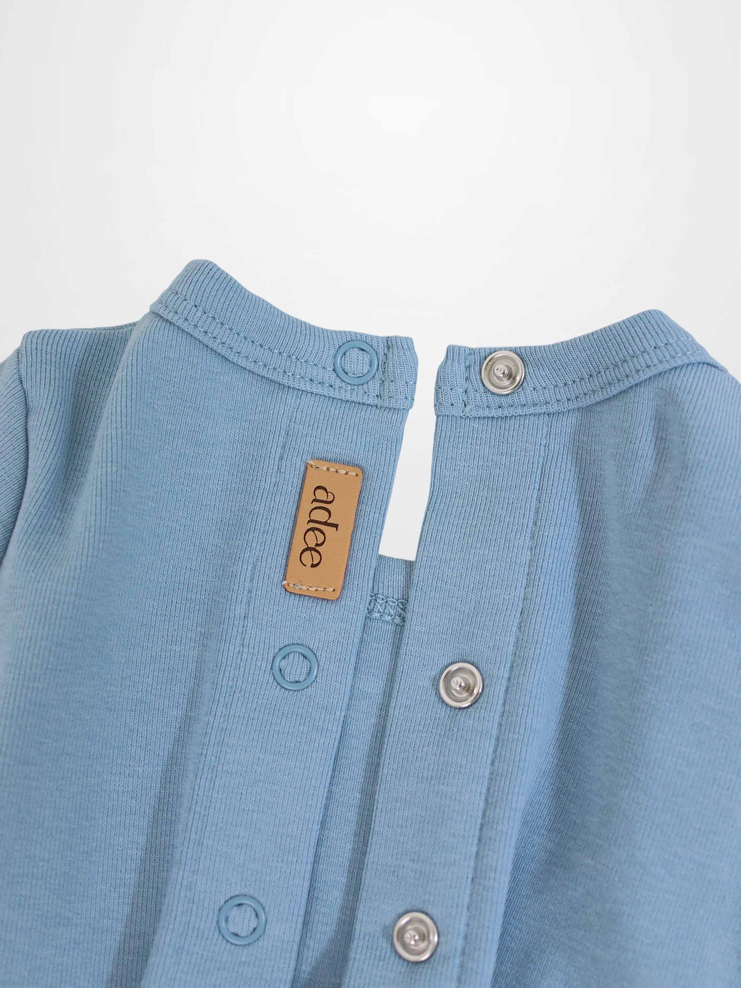 Close-up of a light-blue baby romper neck with snaps, metal grommets, and a tan leather label.