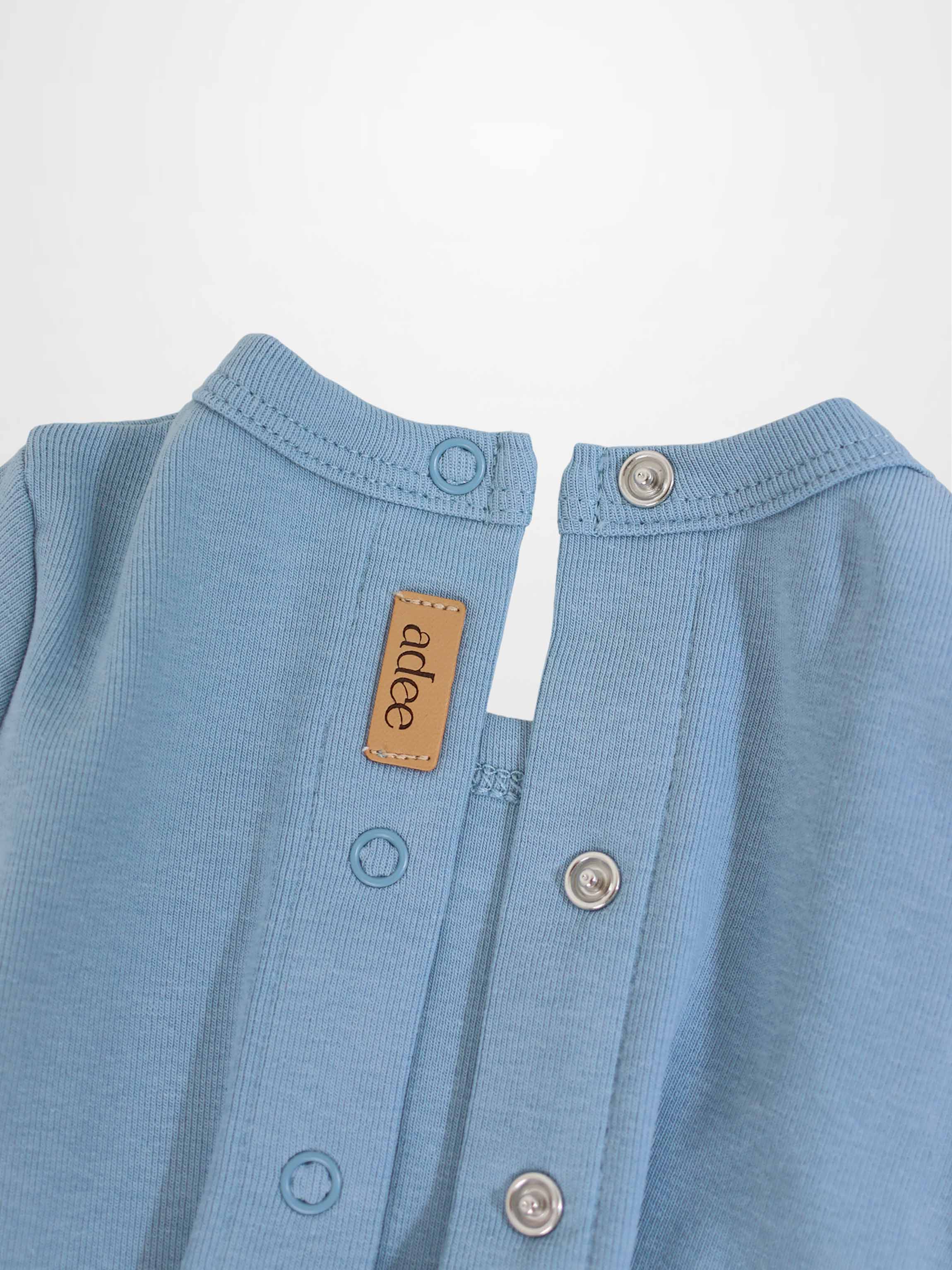 Close-up of a light-blue baby romper neck with snaps, metal grommets, and a tan leather label.