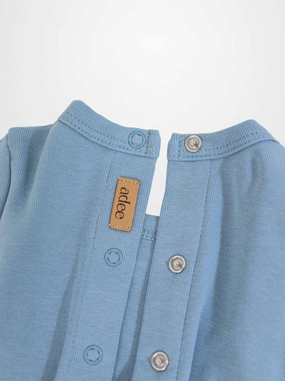 Close-up of a light-blue baby romper neck with snaps, metal grommets, and a tan leather label.