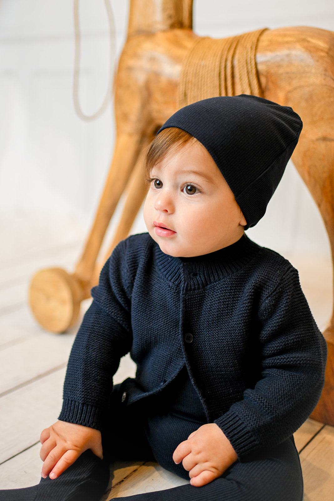 Baby in navy knit mock-neck outfit with matching beanie, showcasing stretchy fabric.