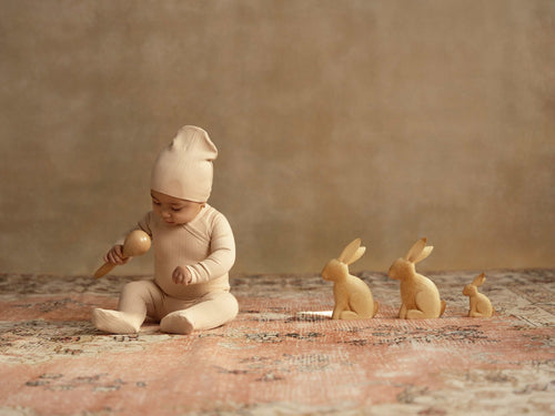 Wide Ribbed Beanie - Light Pink, Adee girls beanies; worn by a baby on a rug with three wooden bunny figurines.