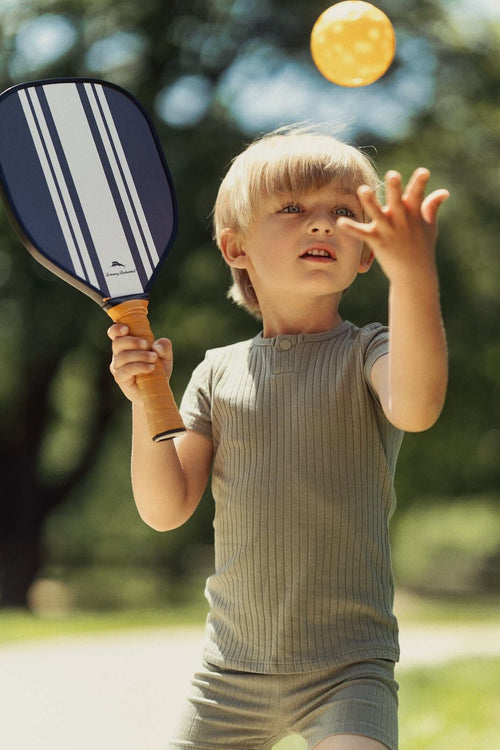 Young child in green wide-ribbed One Snap Henley Short Set, playing paddle ball outdoors.