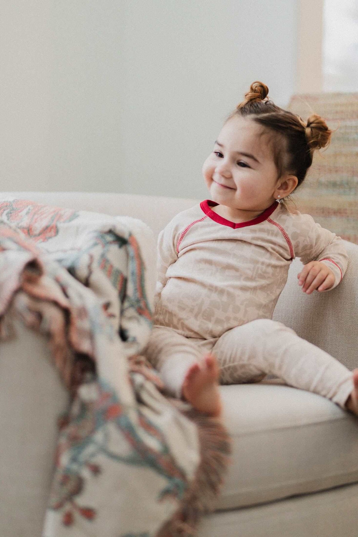 Toddler girl in Abstract Pajamas-Red with neutral pattern and bold red trim, relaxing on couch.