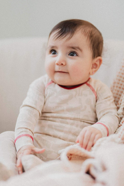 Baby girl in a beige Abstract Print Stretchy- Red jumpsuit with bold red trim and stitching.