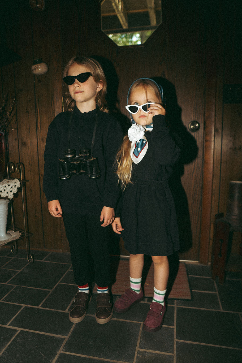 Black denim jumper for girls; two kids in black outfits wearing sunglasses indoors.