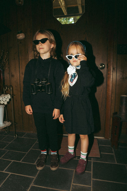 Black denim jumper for girls; two kids in black outfits wearing sunglasses indoors.