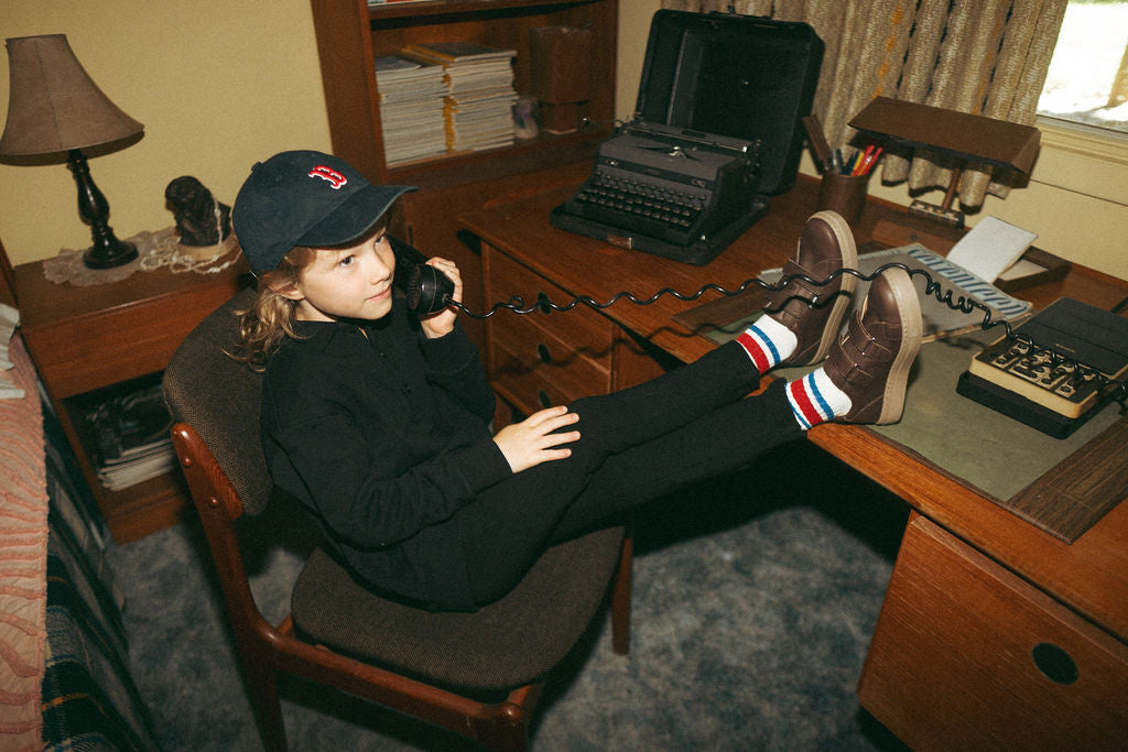 Stretch pants - black; child wearing black pants with striped socks and brown sneakers, feet resting on a desk.