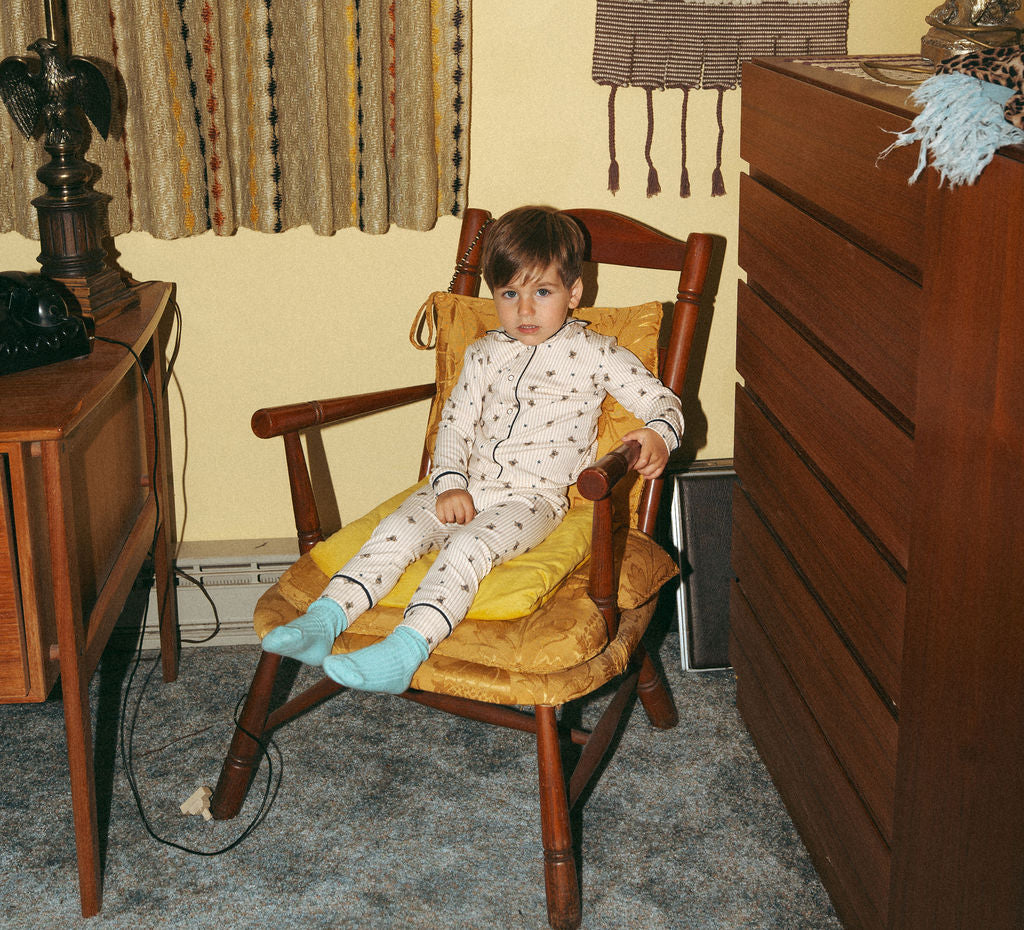 Boys striped bear pajamas in light fabric worn by a child in a wooden rocking chair.